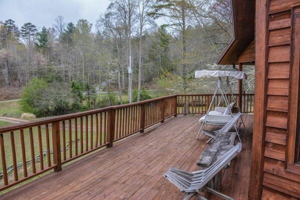 A wooden deck with a railing, a covered seating area, and a view of a forested area.