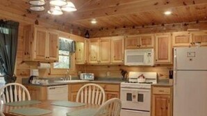 Eine Küche im Blockhausstil mit Holdelementen, einem weißen Kühlschrank, einem Herd und einer Mikrowelle. Ein Holzessttisch mit Stühlen steht ebenfalls dort.