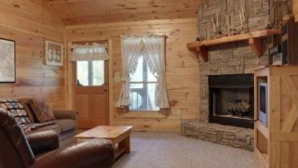 Ein gemütliches Blockhaus-Interieur mit Kamin, Holzwänden, einer Ledersofa und einer Kaminverkleidung aus Stein.