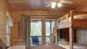 Eine Holzhütte mit Etagenbett, Deckenventilator und Blick ins Freie.