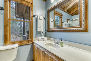 A bathroom with a wooden vanity, a large mirror, and a window with a view of trees. - Twin Peaks 2/malu (Blue Ridge)