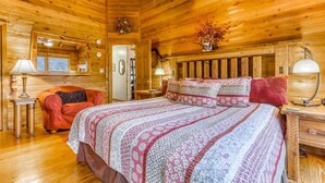 A cozy wooden cabin bedroom with a large bed, two bedside tables, a red chair, and a ceiling fan. - Twin Peaks 2/malu (Blue Ridge)