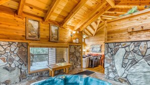 A wooden cabin interior with a stone wall, a hot tub, and a dining area. - Twin Peaks 2/malu (Blue Ridge)