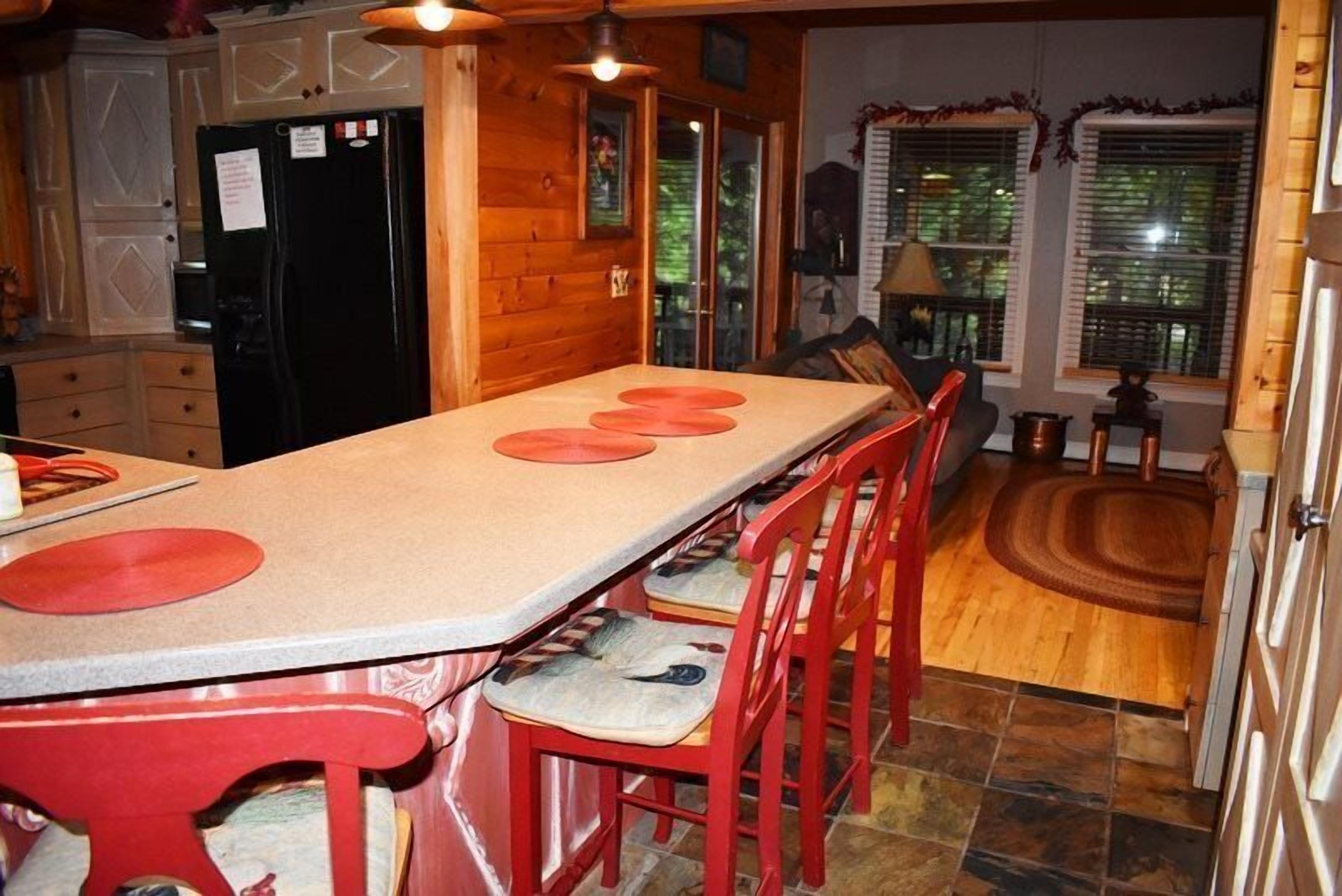 A kitchen with a long island, red chairs, a black refrigerator, and wooden cabinets.
