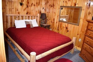 A wooden-framed bed with a red quilt, a small bedside table with a lamp, and a mirror on the wall. - Roosters Roost (Blue Ridge)