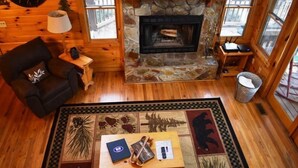 A cozy cabin interior with a stone fireplace, wooden furniture, and a checkered rug. - Serendipity (Blue Ridge)