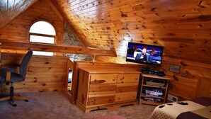 A cozy attic bedroom with a wooden sloped ceiling, a television, a desk, and a comfortable bed. - Serendipity (Blue Ridge)
