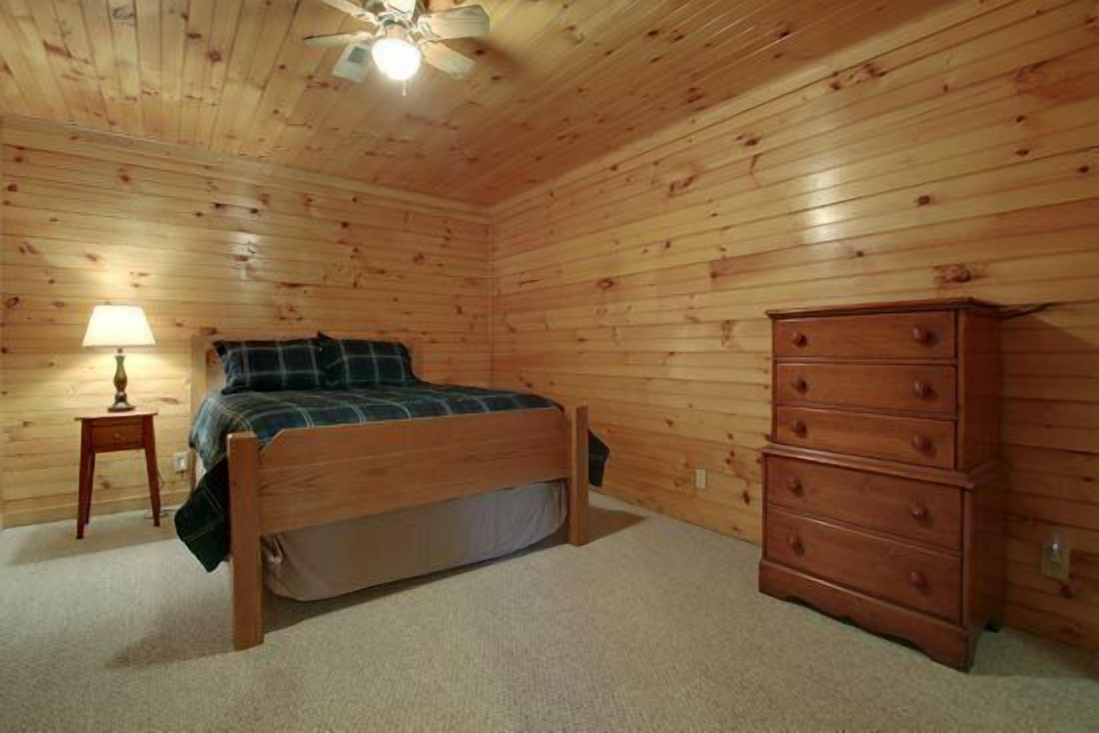 Une chambre aux murs lambrés, avec un lit, une commode et une table de chevet sur laquelle se trouve une lampe.