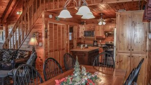 A wooden cabin interior with a dining area, kitchen, and staircase. - Mountain Rivers Lodge (Mineral Bluff)