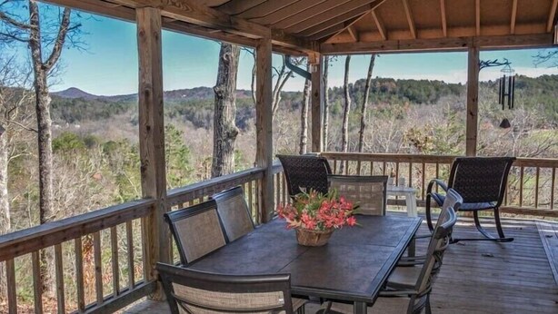 An outdoor wooden deck with a table and chairs, overlooking a forested landscape. - Mountain Rivers Lodge (Mineral Bluff)