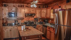 A wooden cabin kitchen with a central island, built-in microwave, stove, and stainless steel refrigerator. - Mountain Rivers Lodge (Mineral Bluff)