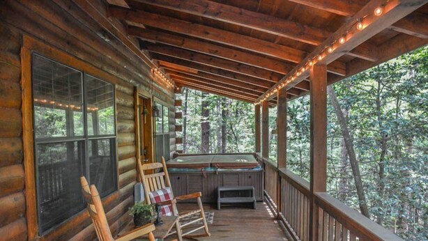A wooden cabin with a porch, large windows, and a seating area with chairs and a bench. - Squirrelled Away (Cherry Log)