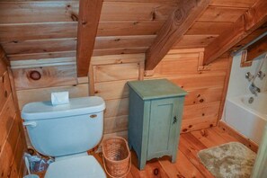 A small, wooden cabin bathroom with a toilet, a cabinet, and a bathtub.
