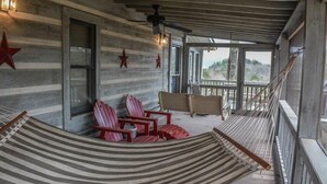 Een overdekt terras met een hangmat, rode Adirondack-stoelen en een houten bank.
