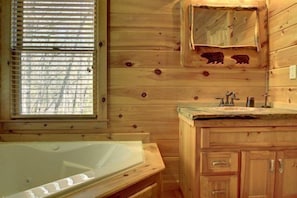 A wooden cabin bathroom with a bathtub, wooden cabinets, and a window with blinds.
