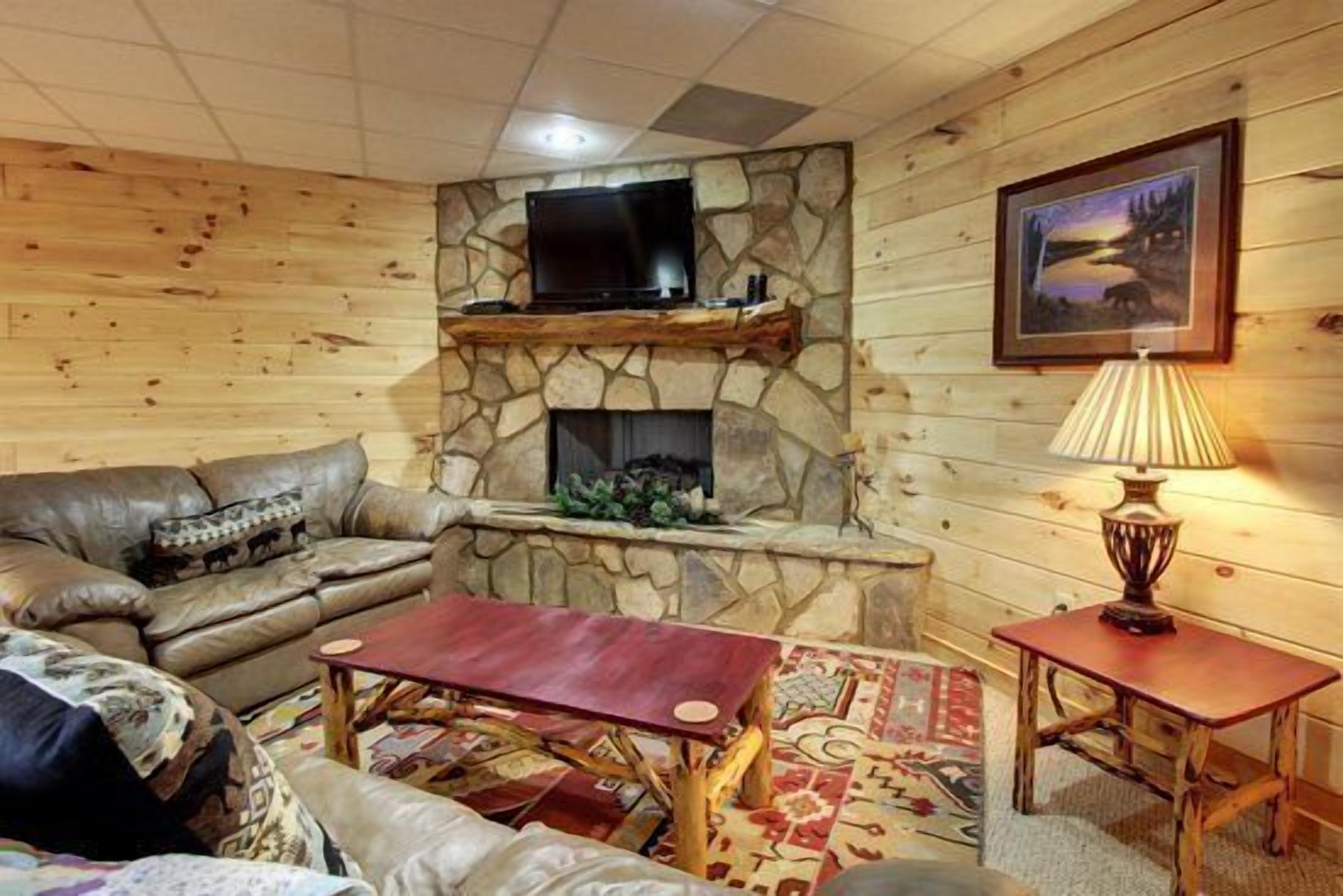 A cozy living room with a stone fireplace, a television mounted above it, a comfortable sofa, a small wooden table, and a lamp on a side table.