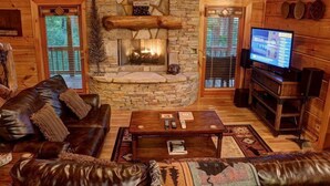 Interior acogedor de una cabaña con chimenea de piedra, sofá de cuero y televisor.