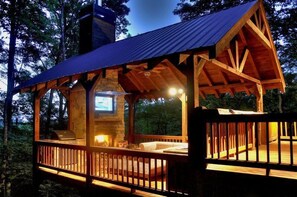 A rustic cabin with a stone fireplace, wooden deck, and a large TV screen. - Moon Shadow Overlook (Blue Ridge)