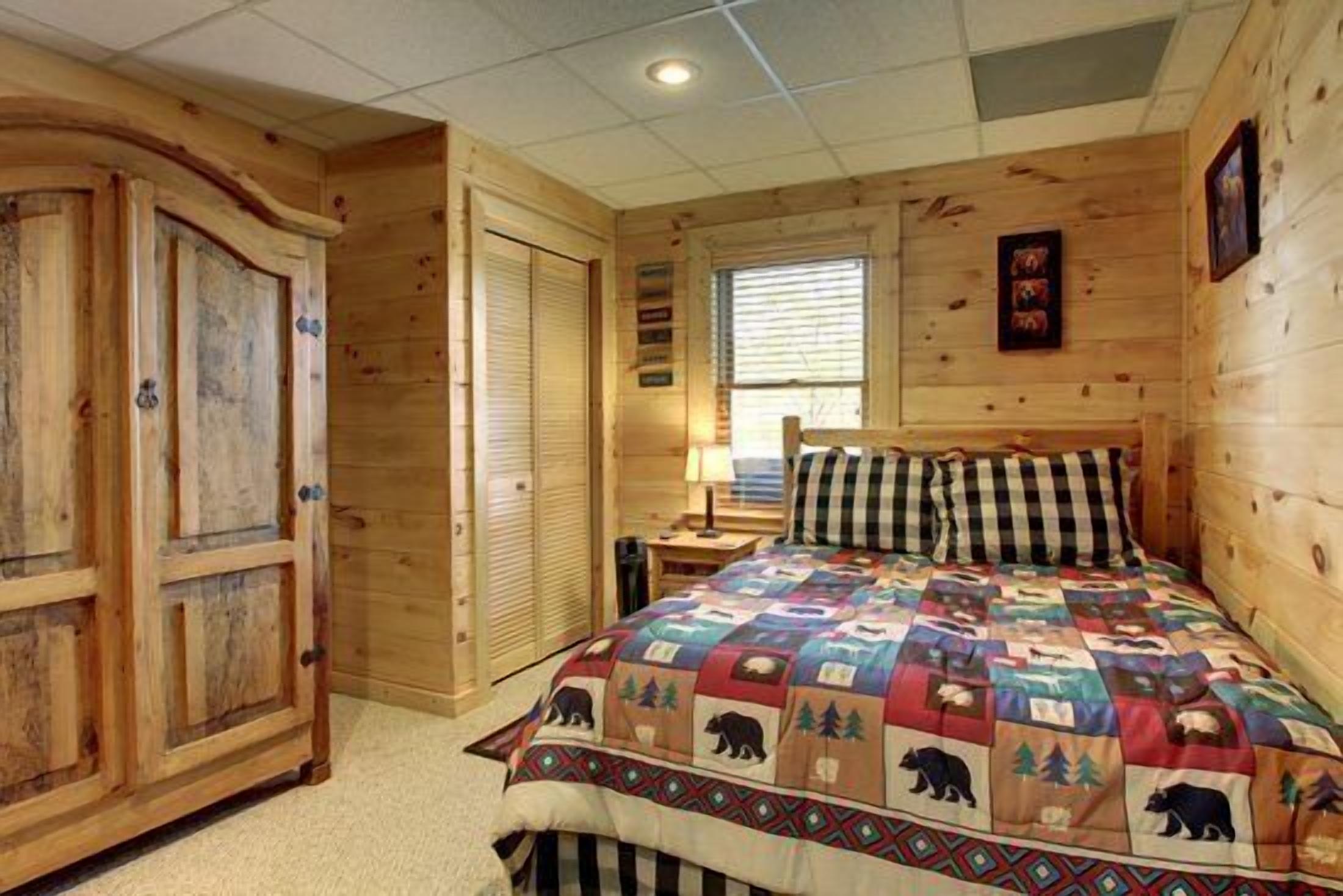A wooden cabin-style room with a large bed, a wooden wardrobe, and a window with blinds.