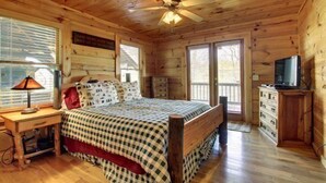 Un dormitorio de cabaña de madera con una cama, un escritorio, un aparador y un ventilador de techo.