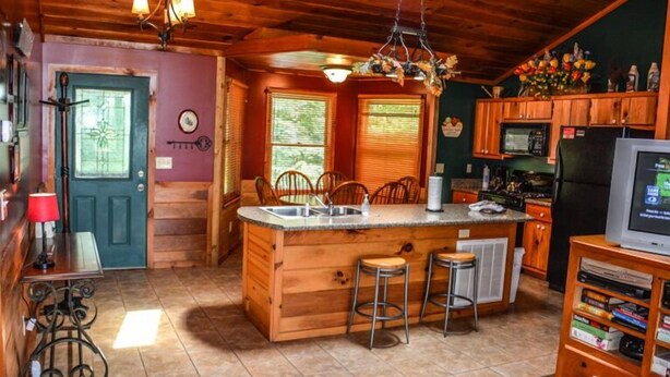 A cozy cabin-style kitchen with wooden cabinets, a central island with stools, a built-in microwave, and a refrigerator. - Picabo (Blue Ridge)