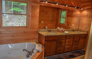 Un baño de cabaña de madera con una bañera grande, encimera de granito y armarios de madera.