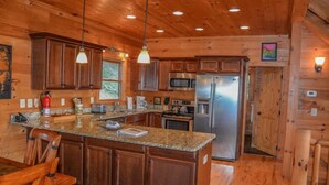 A wooden cabin-style kitchen with granite countertops, stainless steel appliances, and pendant lighting. - Dream Catcher (Morganton)