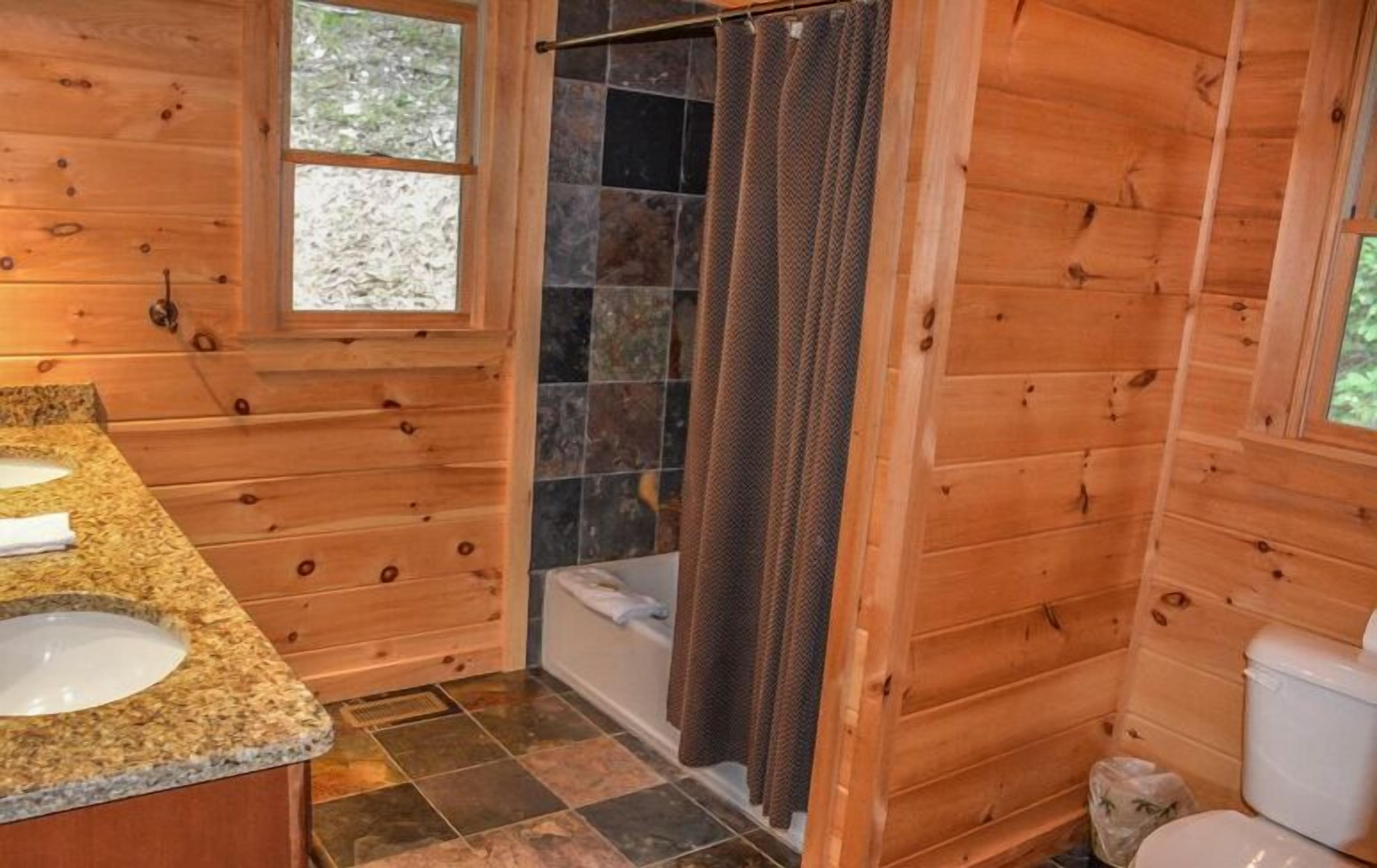 Une salle de bain rustique, aménagée dans une cabane en bois, avec une douche, deux lavabos et des toilettes.