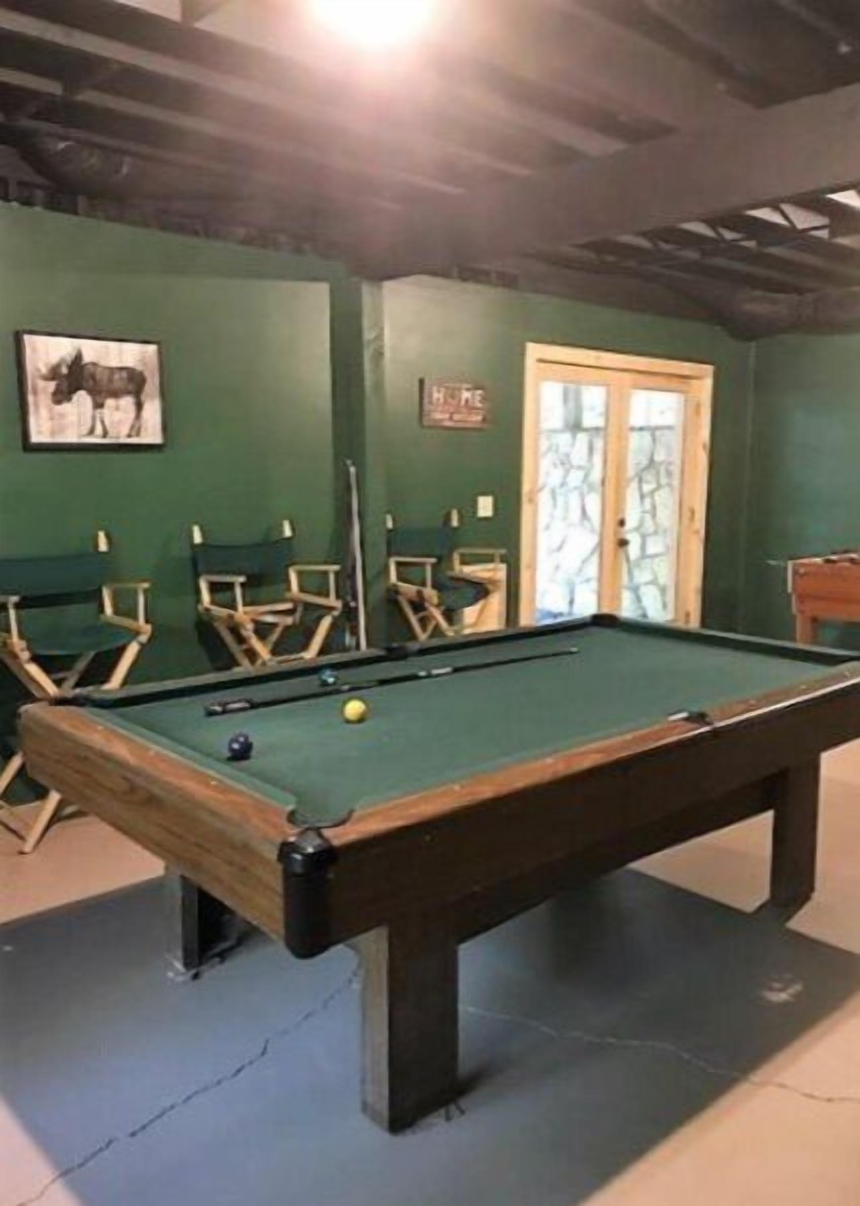Une table de billard recouverte d’un drap vert, entourée de murs verts et de chaises en bois.