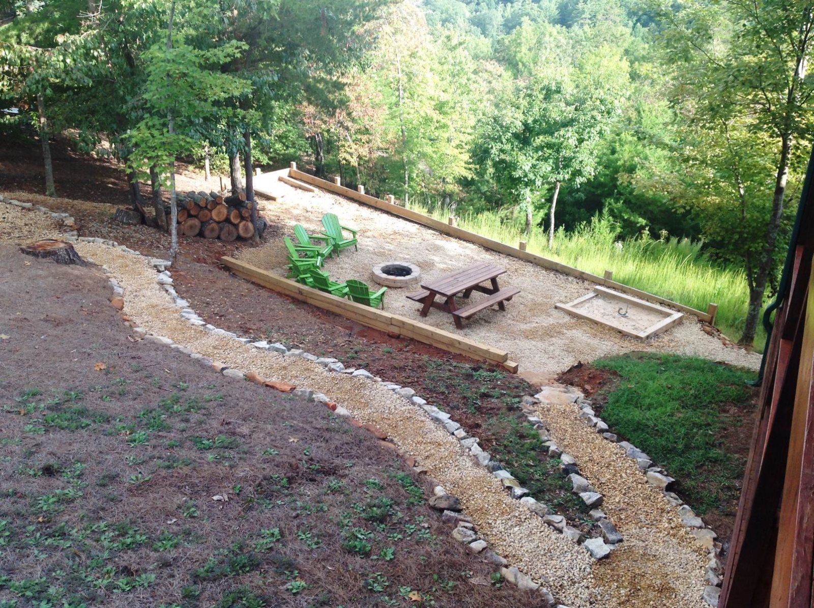 A patio area with a wooden table and chairs, surrounded by a gravel path and a wooden deck.