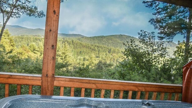 Uma banheira de hidromassagem com deck de madeira e vista panorâmica de uma cadeia montanhosa coberta por floresta.