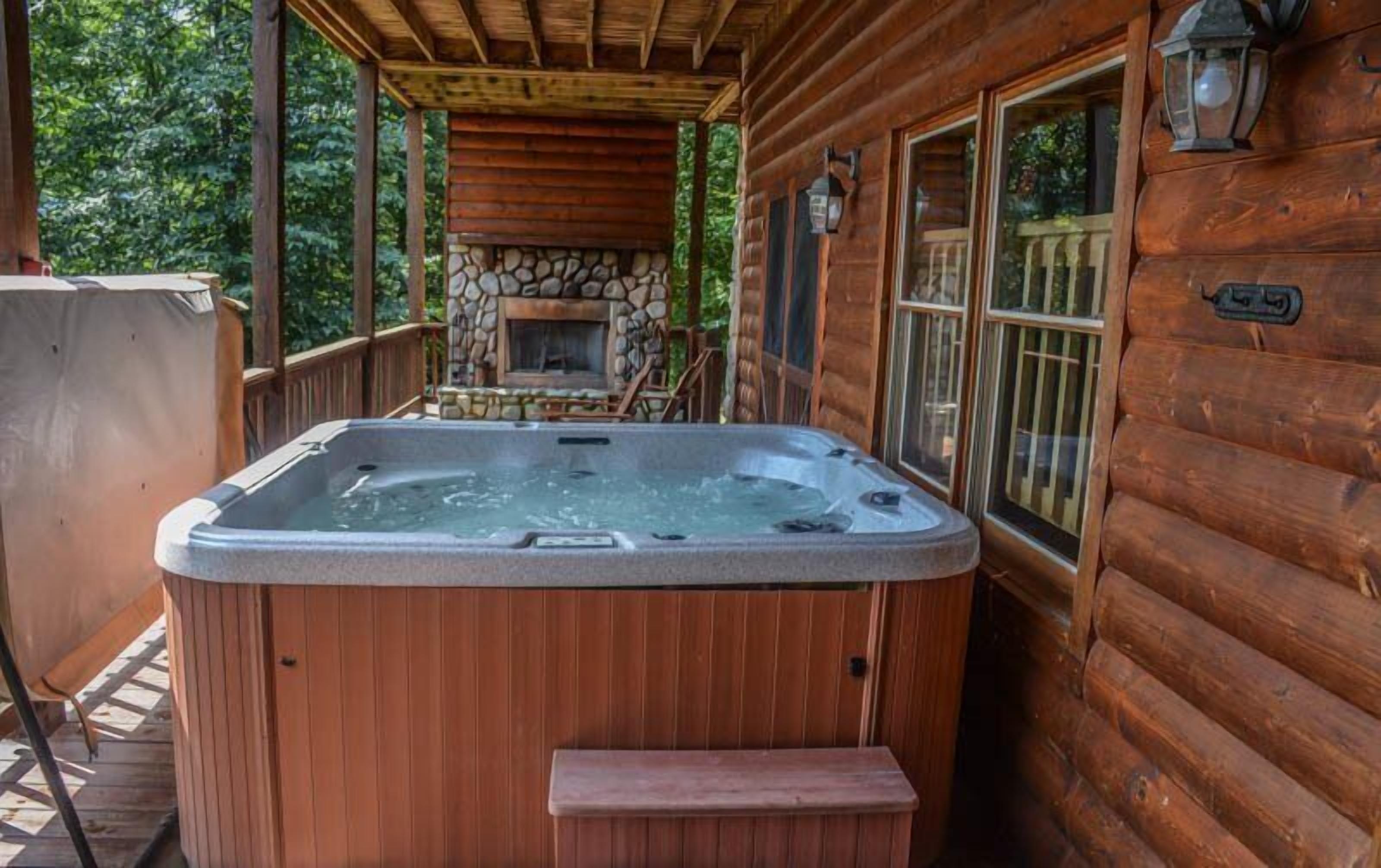 A wooden cabin with a hot tub, stone fireplace, and large windows.