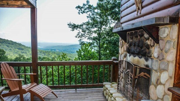 Une terrasse en bois avec une cheminée en pierre, une chaise en bois et une vue panoramique sur un paysage boisé.