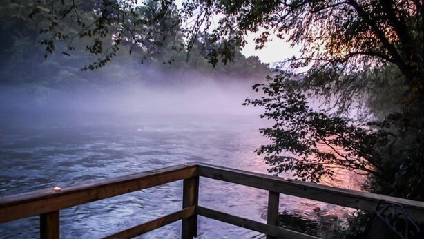 A wooden deck overlooking a river with mist and trees in the background. - Misty River (Mineral Bluff)