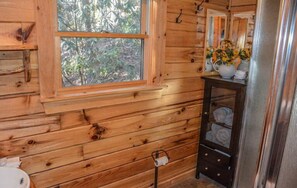 A wooden cabin bathroom with a window, a sink, a mirror, and a towel rack.