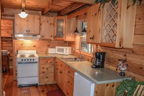A wooden cabin kitchen with a stove, microwave, sink, and coffee maker.