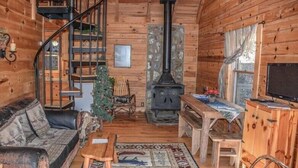 En mysig stuga med en spiraltrappa, en steneldstad, en soffa i trä, ett litet bord och en tv.