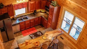 Cozinha estilo cabana com armários de madeira, uma ilha central com banquetas, geladeira e uma janela grande.