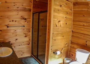 A wooden cabin bathroom with a shower, sink, toilet, and a towel rack. - The Great Escape (Morganton)