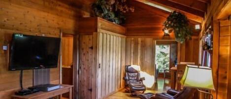 A wooden cabin interior with a TV, two chairs, a bench, and a lamp.