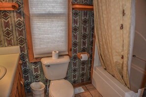 Un baño con inodoro, rollo de papel higiénico, un cesto de basura y cortina de ducha.