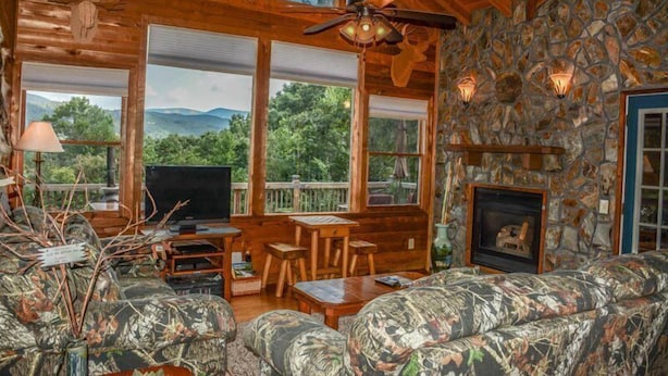 A cabin interior with a stone wall, wooden ceiling, a fireplace, a TV, and a sofa. - Okeana (Blue Ridge)