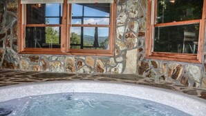 A stone-walled hot tub area with a view of the outdoors through a window. - Okeana (Blue Ridge)