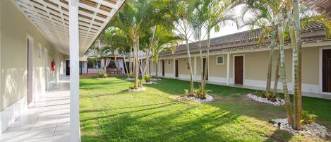 Un corredor cubierto con varias habitaciones, palmeras y un césped bien cuidado.