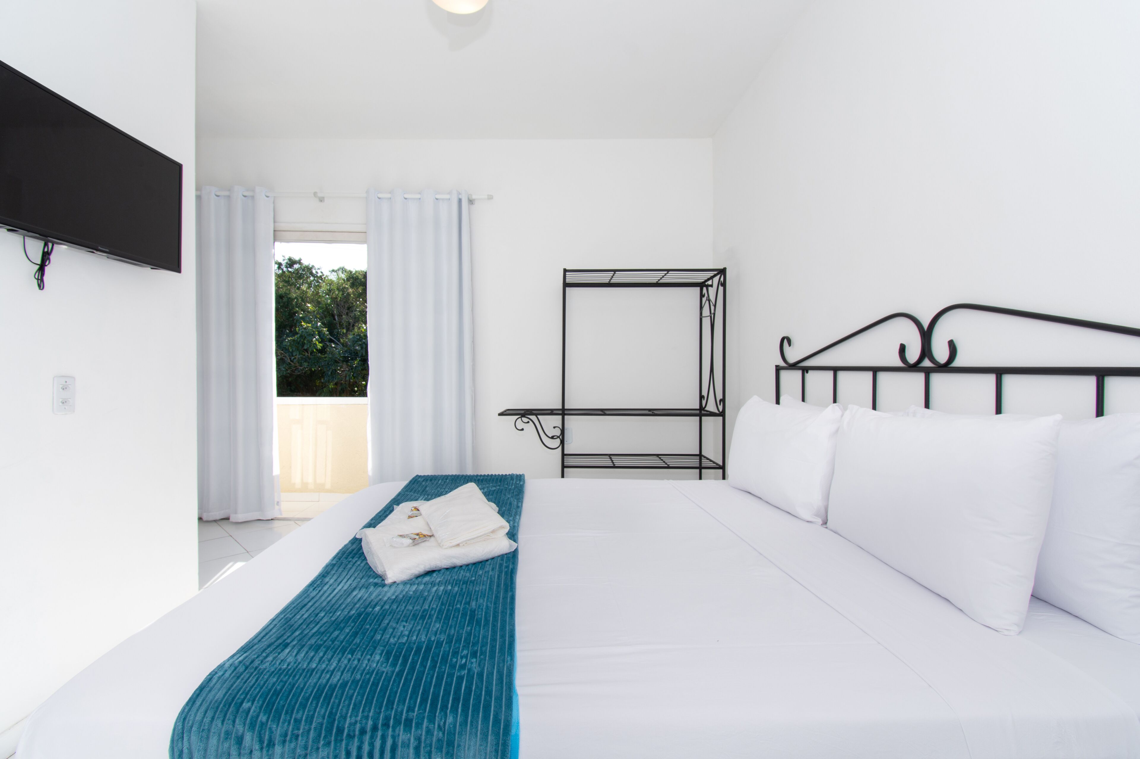 A hotel room with a bed, a blue blanket, white pillows, a metal bunk bed, and a TV mounted on the wall.