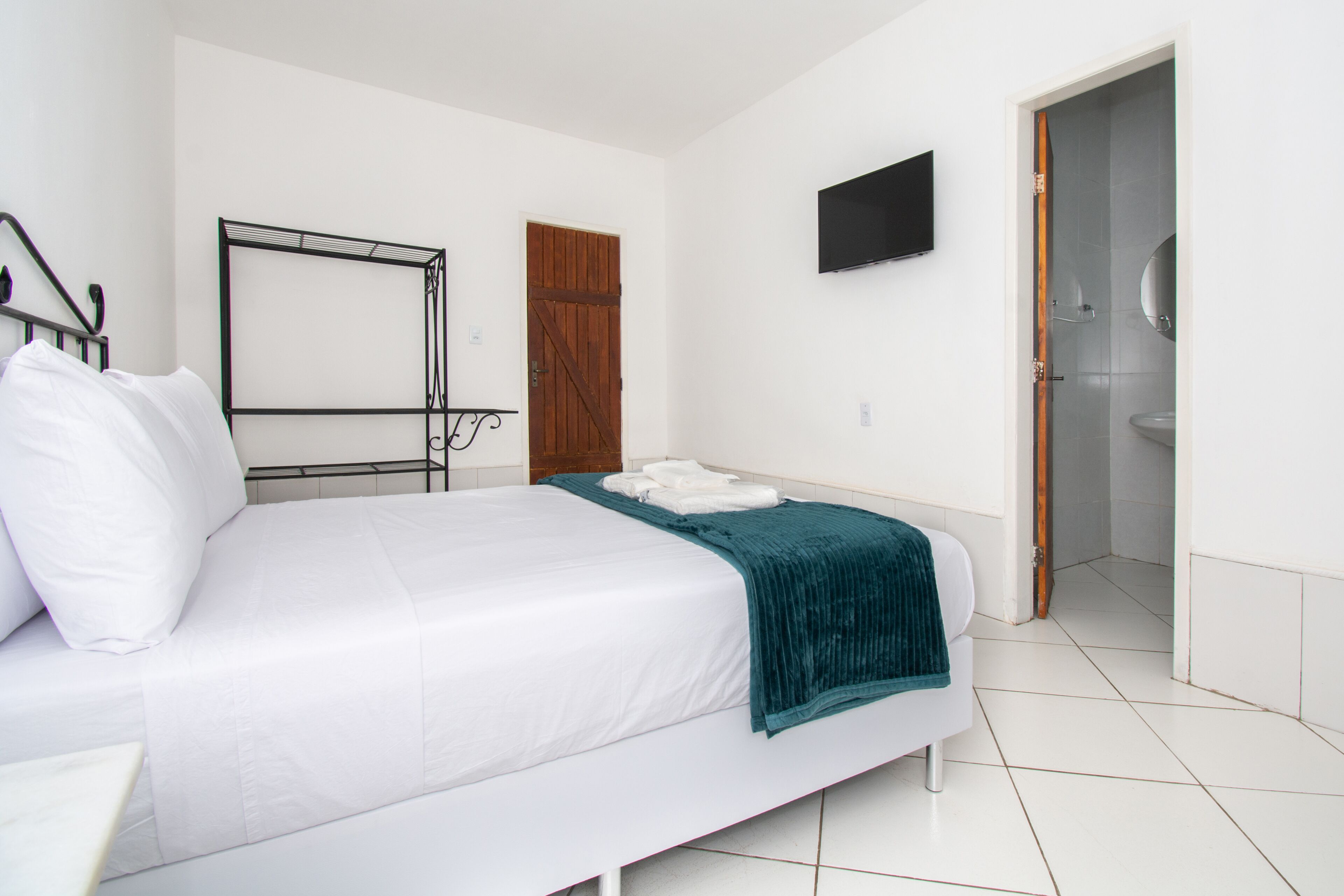 A bedroom with a bed, a TV mounted on the wall, a wooden door, and a bathroom visible through an open door.