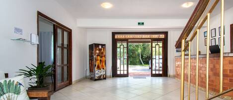 A spacious lobby with a wooden bench, a potted plant, and a coffee machine.