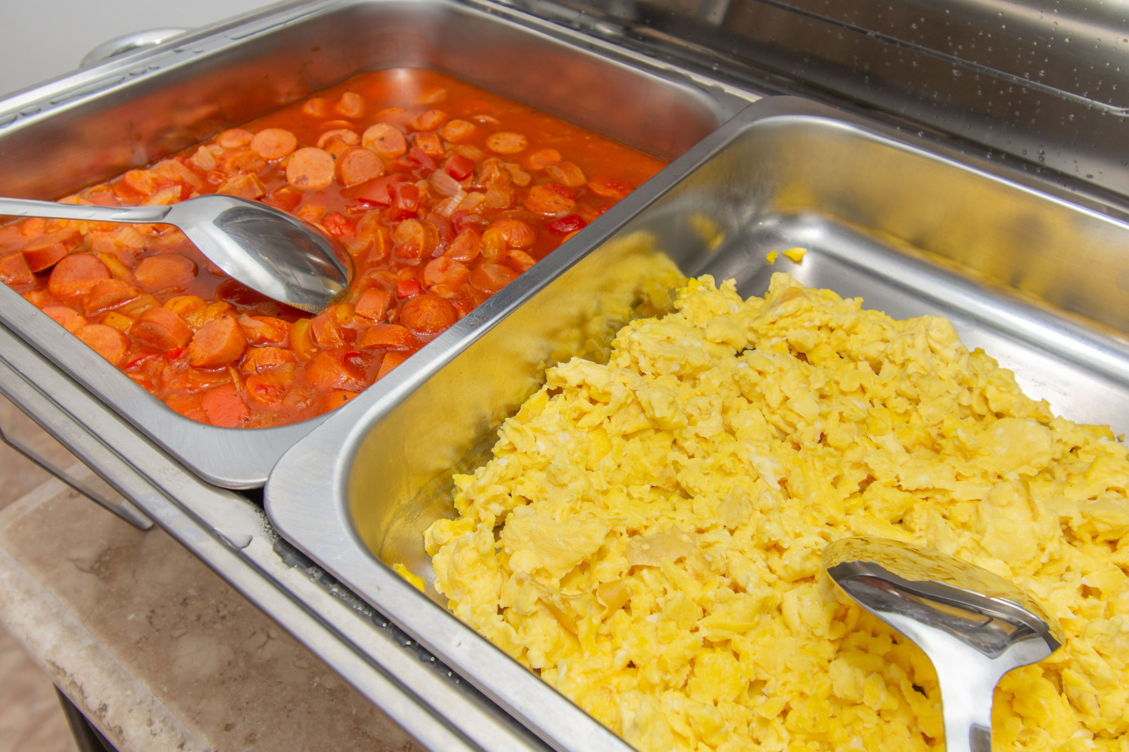 A buffet with two trays of food: one with scrambled eggs and another with beans and carrots.