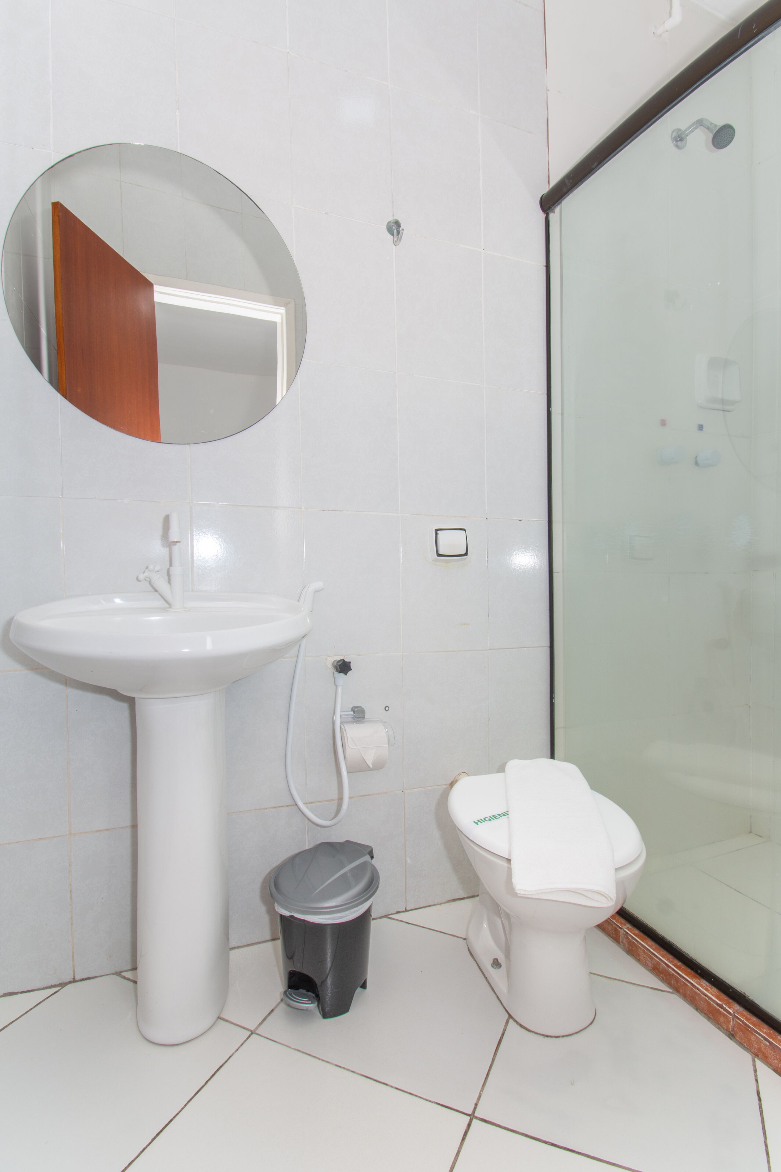 A bathroom with a white sink, a toilet, a trash bin, and a glass shower enclosure.