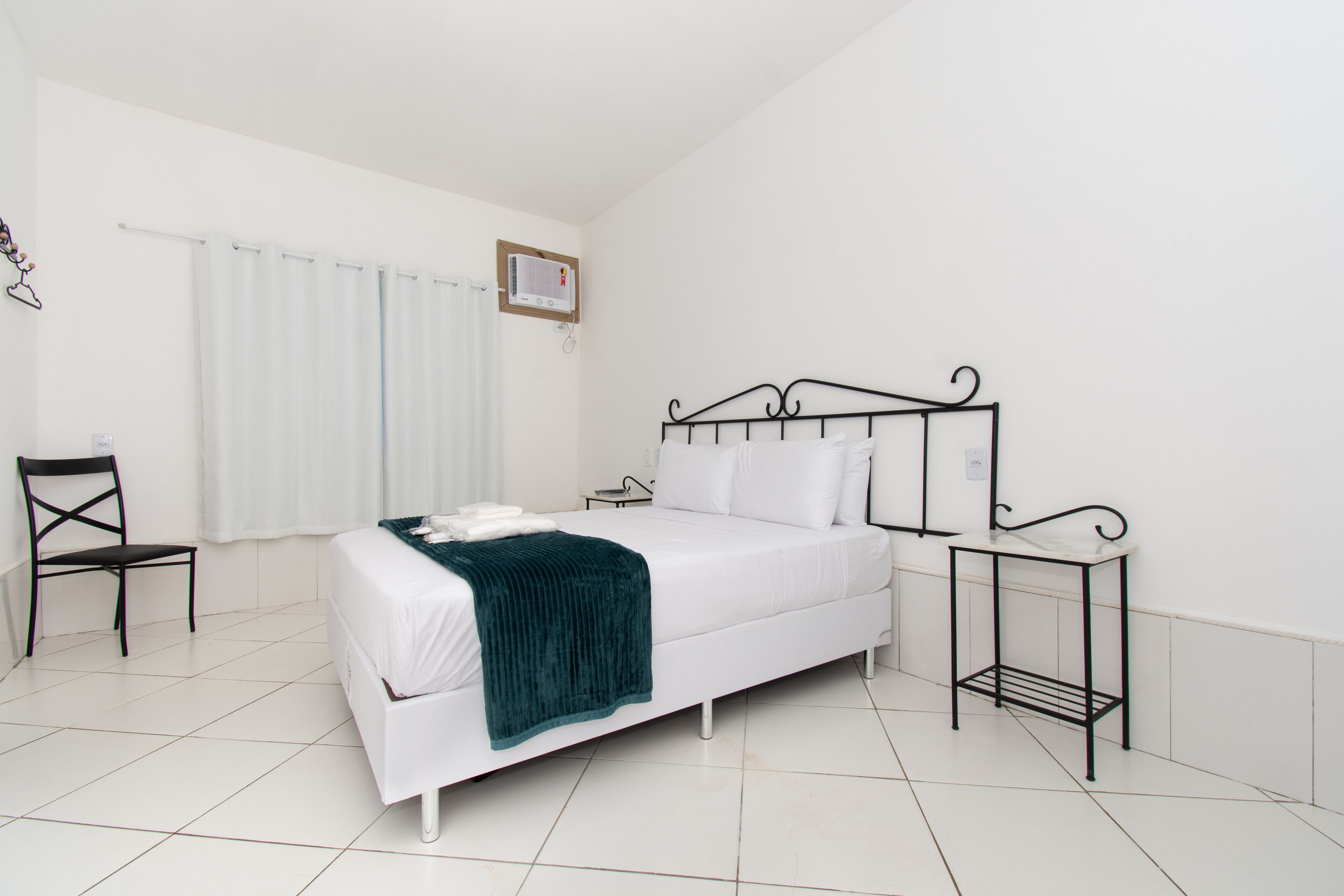 A bedroom with a bed, a chair, a bedside table, and a window with curtains.